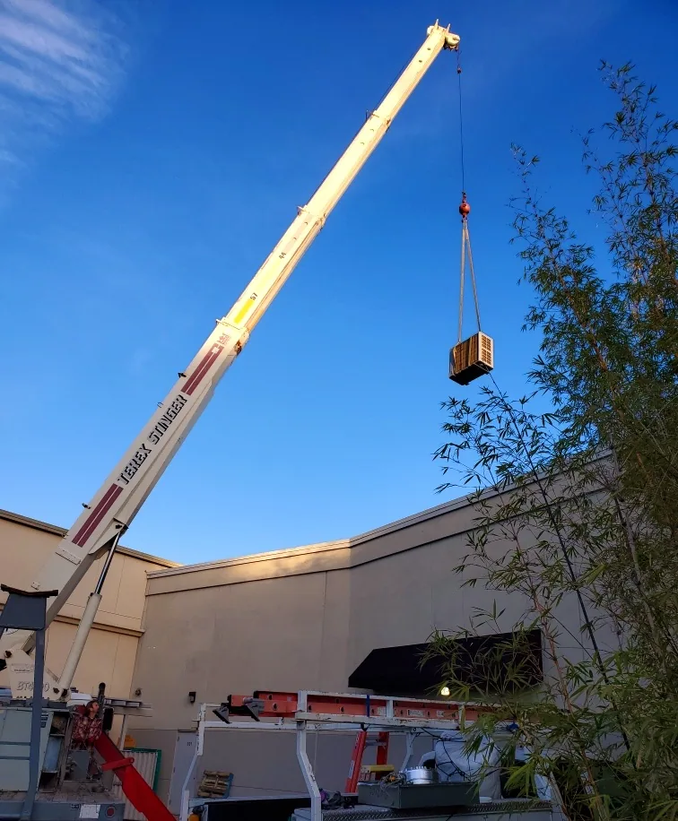Crane lifting a commercial rooftop HVAC unit into place